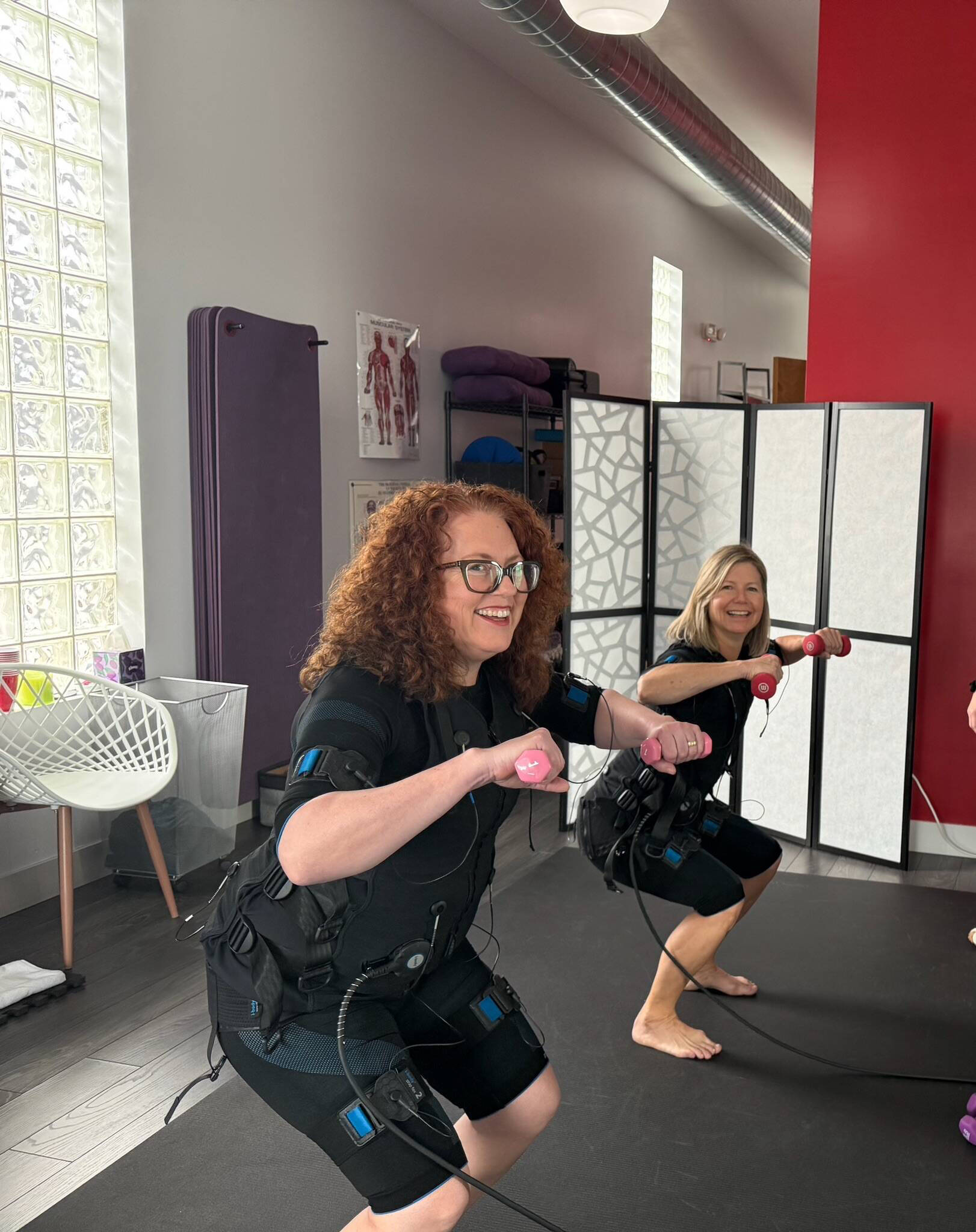 Two women training with EMS suits and pink dumbbells at Electric Body studio